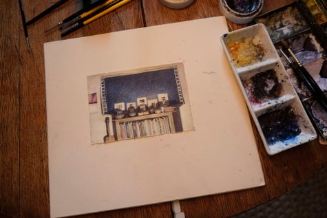 The image shows the drawing mounted to board resting on the drawing table beside watercolors, brushes, and porcelain mixing palette with gum arabic.